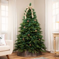 a decorated christmas tree in a living room with white walls and wooden flooring, gold ornaments on the top