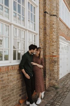 a man and woman standing next to each other in front of a brick building with white windows