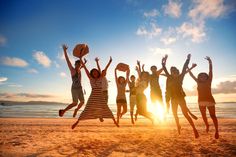 a group of people jumping up in the air on a beach at sunset or sunrise