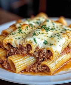 a white plate topped with lasagna covered in meat and cheese on top of sauce