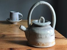 a tea kettle sitting on top of a wooden table next to a cup and saucer