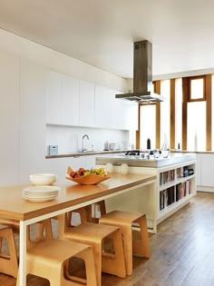 a kitchen with white walls and wooden floors has an island table surrounded by stools