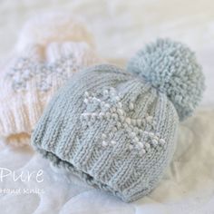 two knitted hats sitting on top of a bed