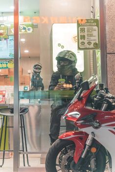 a man sitting on a motorcycle in front of a store window while looking at his cell phone