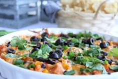 a white bowl filled with black olives and green garnish next to chips