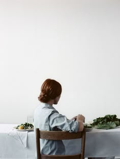 a woman sitting at a table in front of a plate of food with greens on it