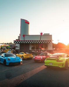 several different colored cars parked in front of a fast food restaurant with the sun setting behind them