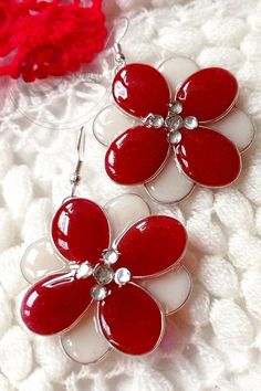 two red and white flower shaped earrings on top of a white blanket next to a piece of fabric