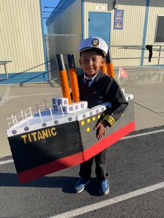 a young boy in uniform holding a model of a boat