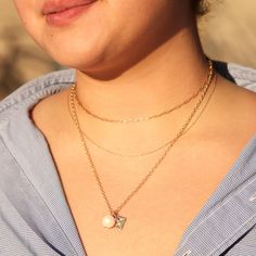 A woman with her hair pulled away from her tanned skin. She wears a blue button down. She wears three gold necklaces. Though you can only see her neck and a bit of her chin, the warm glow and her soft smile makes it seem like she is watching the sunset on a beautiful day. Yellow Gold Pearl Chain Necklace, Elegant Pendant Layered Necklace With Chain, Elegant Everyday Double Chain Charm Necklaces, Elegant Charm Necklaces With Adjustable Chain, Elegant Everyday Double Chain Charm Necklace, Elegant Charm Necklace With Delicate Chain, Elegant Everyday Charm Necklace With Double Chain, Elegant Gold Chain Pendant Charm Necklace, Elegant Gold Chain Charm Necklace With Pendant