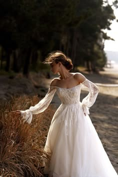 a woman in a wedding dress is standing on the beach with her arms out and looking down