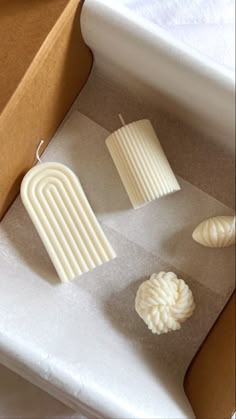 three white candles sitting on top of a table next to a brown box and paper