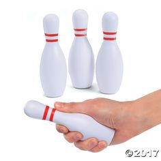 a hand holding a white bowling ball and three pins in front of it on a white background