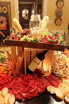 an assortment of food is displayed on a table with wine bottles and breadsticks