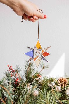 a hand holding an ornament on top of a christmas tree with pine cones