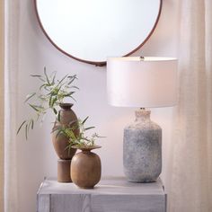 two vases and a lamp on a table in front of a mirror with curtains