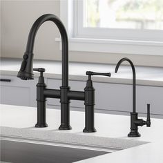 a kitchen sink with two black faucets and a window in the back ground