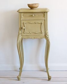 an old fashioned table with a bowl on it's top, against a white wall