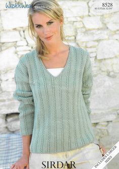 a woman wearing a green sweater and tan pants standing in front of a stone wall