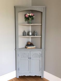 a gray china cabinet with flowers on top and bookshelf in the corner next to it