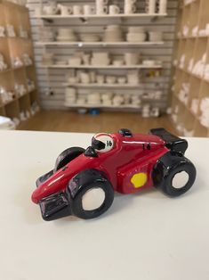 a red toy race car sitting on top of a white table next to shelves filled with boxes