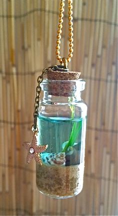 a glass jar filled with sand and sea shells hanging from a gold chain on a bamboo wall