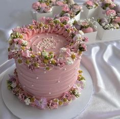 there is a pink cake with flowers on the top and small cupcakes behind it