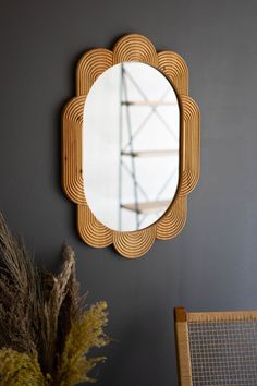 a mirror hanging on the wall next to a chair and vase with dried grass in it