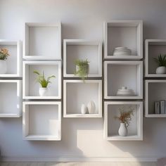 several white shelves with plants and vases on them against a wall in an empty room