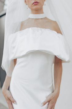 a woman in a white wedding dress with a veil over her head and hands on her hips