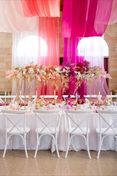 the table is set with white chairs and pink drapes