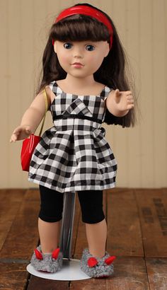 a doll with brown hair and blue eyes wearing black and white checkered dress holding a red purse