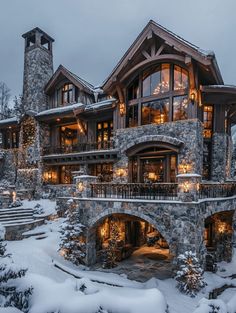 a large stone house covered in snow and lit up with christmas lights on the windows