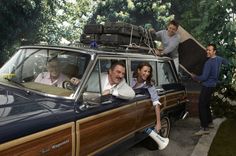 three people sitting in the back of a car with two men standing next to them