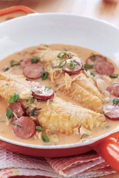 a white bowl filled with soup and meat on top of a wooden table next to a red handled utensil