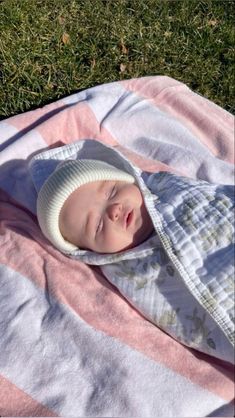 a baby laying on top of a pink and white blanket covered in a knitted hat