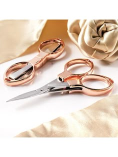 three pairs of scissors sitting next to each other on a white surface with satin material in the background