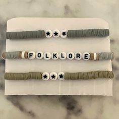 three bracelets that say folklore and are made out of beads with black stars on them