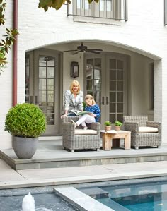 a woman and child sitting on chairs in front of a house with a swimming pool