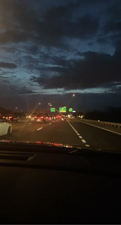 cars driving down the highway at night with dark clouds in the sky and lights on