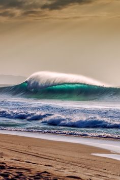 a large wave is coming in to the shore on a cloudy day at the beach