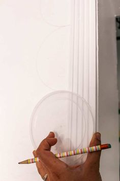 a person holding two pencils in front of a white wall with circles on it