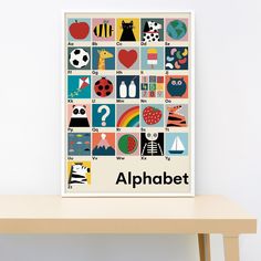 an alphabet poster is displayed on a wooden table in front of a white wall,