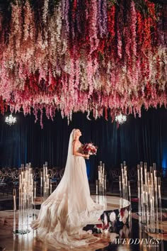 the bride is standing in front of an elaborate floral arrangement with candles and flowers hanging from the ceiling