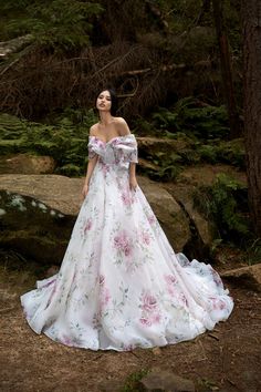 a woman in a white dress standing next to trees and rocks with her hands on her hips