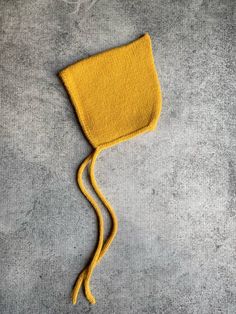 a yellow knitted hat laying on top of a gray surface next to a string