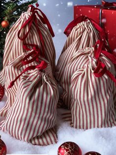 two red and white striped bags sitting next to a christmas tree with presents in the snow