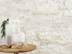 a white vase sitting on top of a wooden table next to a wall covered in stone tiles