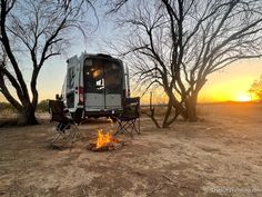 a camper van sitting next to a fire in the middle of a field at sunset