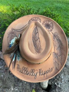 Hand burned sunflower and feather Hillbilly Hippie hat. This beauty is perfect for your next concert, dinner date or any special occasion. It's simply stunning. Hats are one size fits all with a drawstring to adjust sizing. Bohemian Felt Hat For Western-themed Summer Events, Summer Bohemian Felt Hat For Western-themed Events, Bohemian Felt Hat For Summer Western-themed Events, Hippie Brimmed Hat For Country Events, Custom Summer Fedora For Country Events, Top Hat For Kentucky Derby And Country Events, Flat Brim Hats With Feathers For Country Events, Bohemian Costume Hats With Short Brim For Western-themed Events, Bohemian Short Brim Costume Hat For Western-themed Events